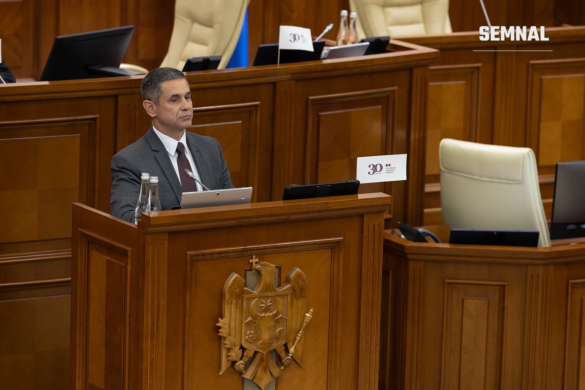 Anatolie Nosatîi în costum gri, la tribuna din sala de ședințe, cu stema Moldovei pe pupitru. (Foto: Parlamentul Republicii Moldova | Pagina oficială)