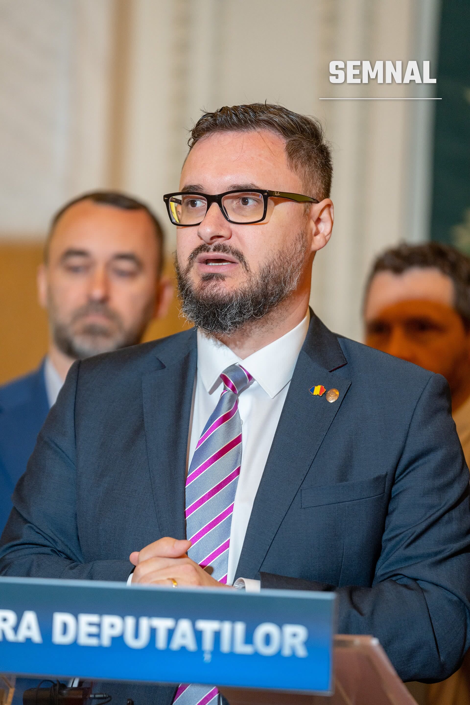 Dan Tanasă vorbind la un pupitru al Camerei Deputaților, în costum bleumarin, cu cravată în dungi mov și un ac cu tricolorul României. (Foto: Dantanasa)