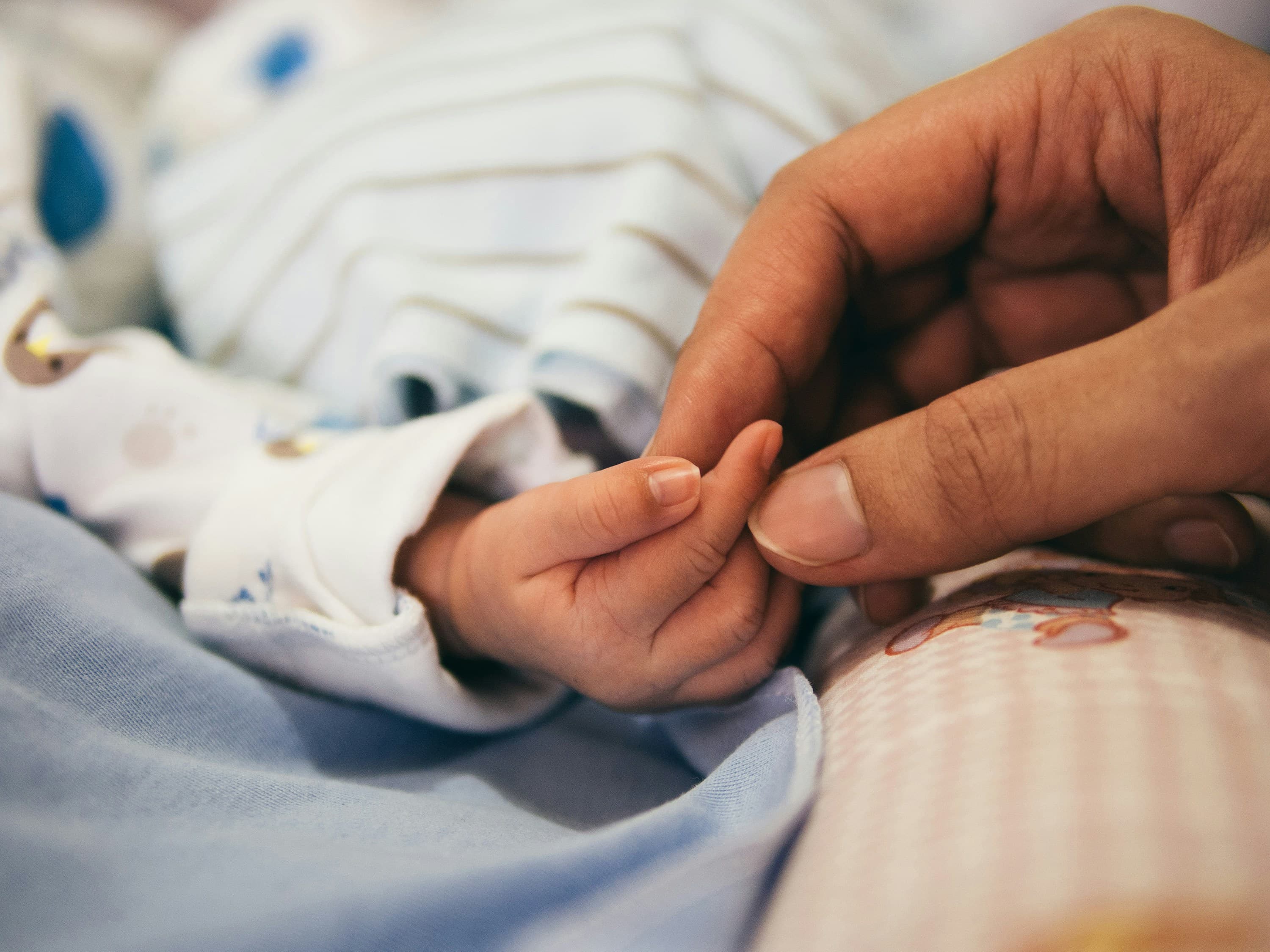 Mână de adult ținând delicat degetul unui copil, simbol al îngrijirii medicale