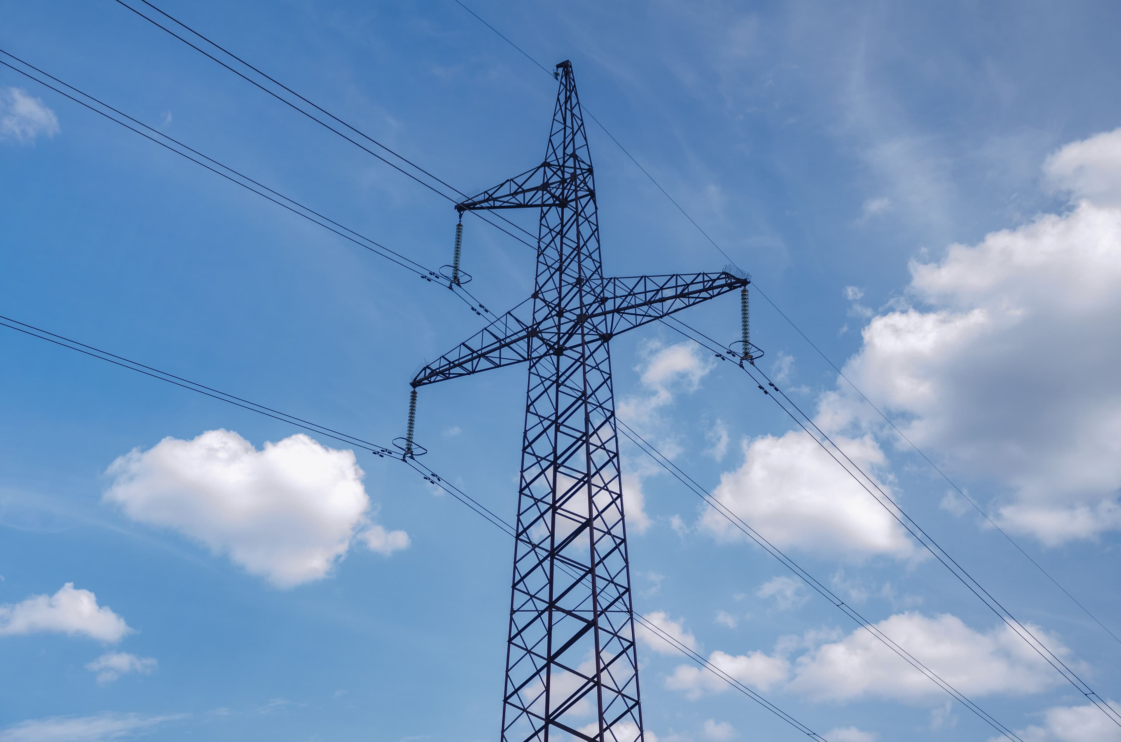 Stâlp de înaltă tensiune pentru transportul energiei electrice, pe fundal de cer albastru cu nori