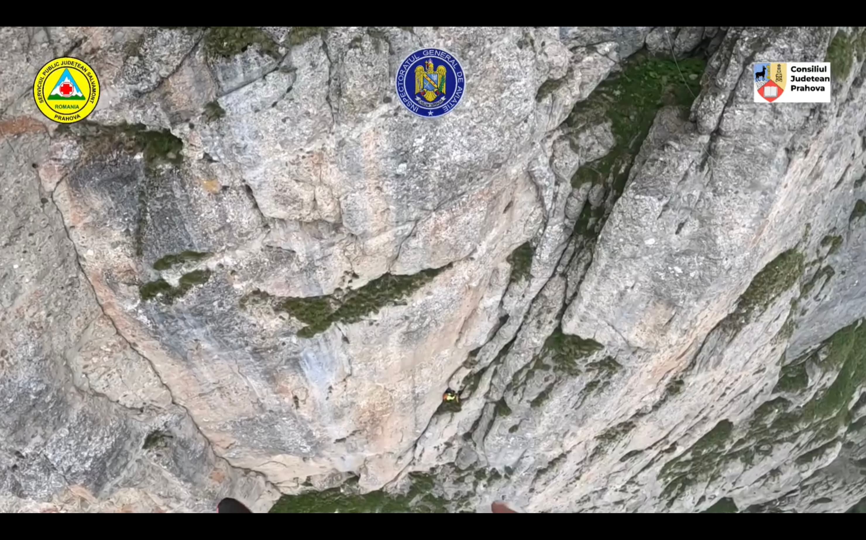 Vedere de pe casca unui salvamontist către peretele vertical al Văii Albe, cu un alpinist echipat agățat de stâncă