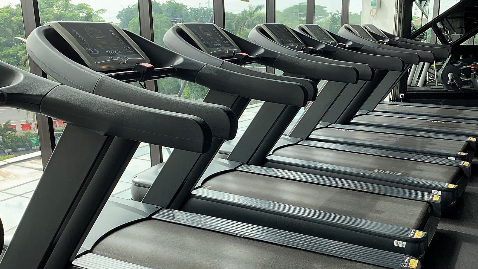 Rând de benzi de alergare într-o sală de fitness, lângă un perete de sticlă