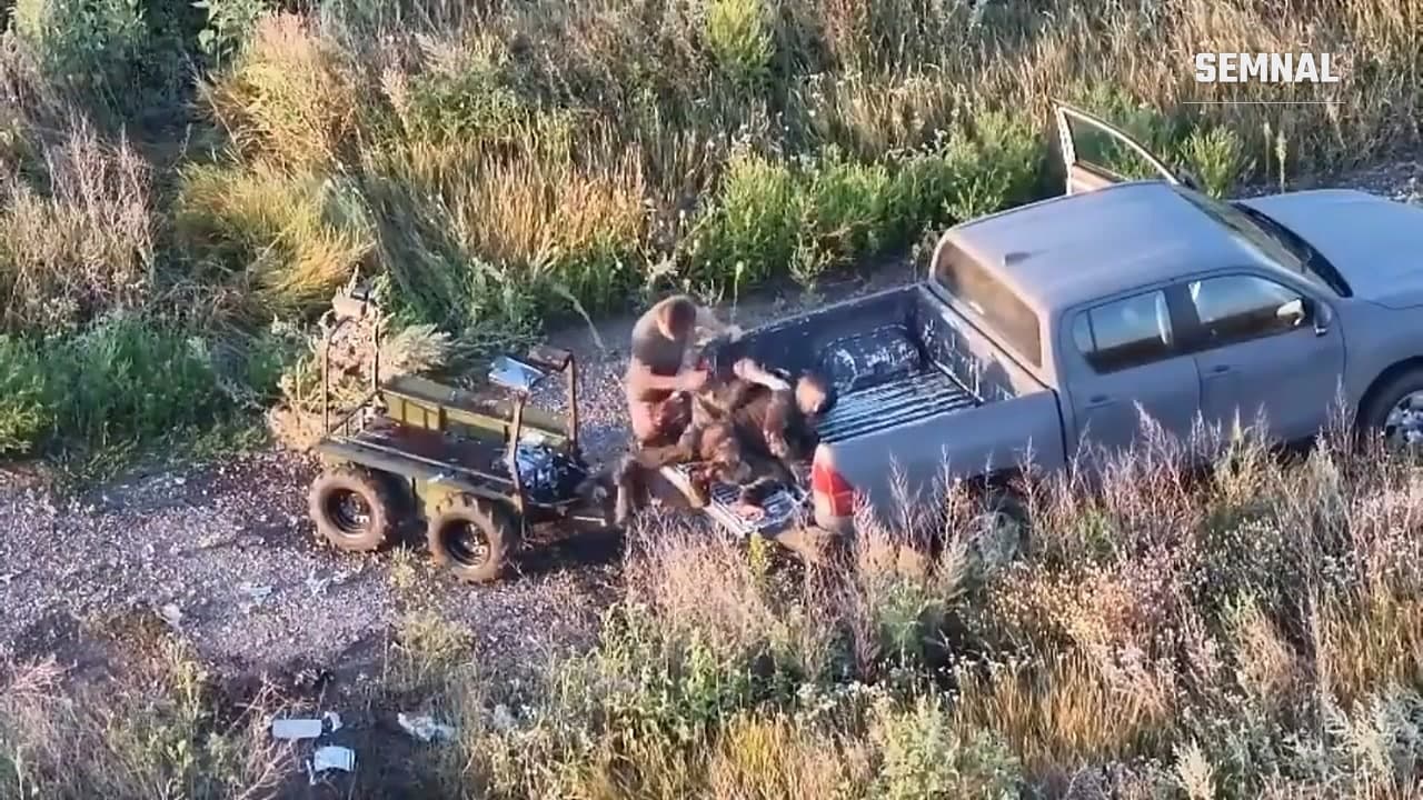 Cadru filmat din dronă: un comandant ucrainean transferă doi soldați răniți dintr-un robot terestru avariat în bena unui pickup, pe un drum de câmp