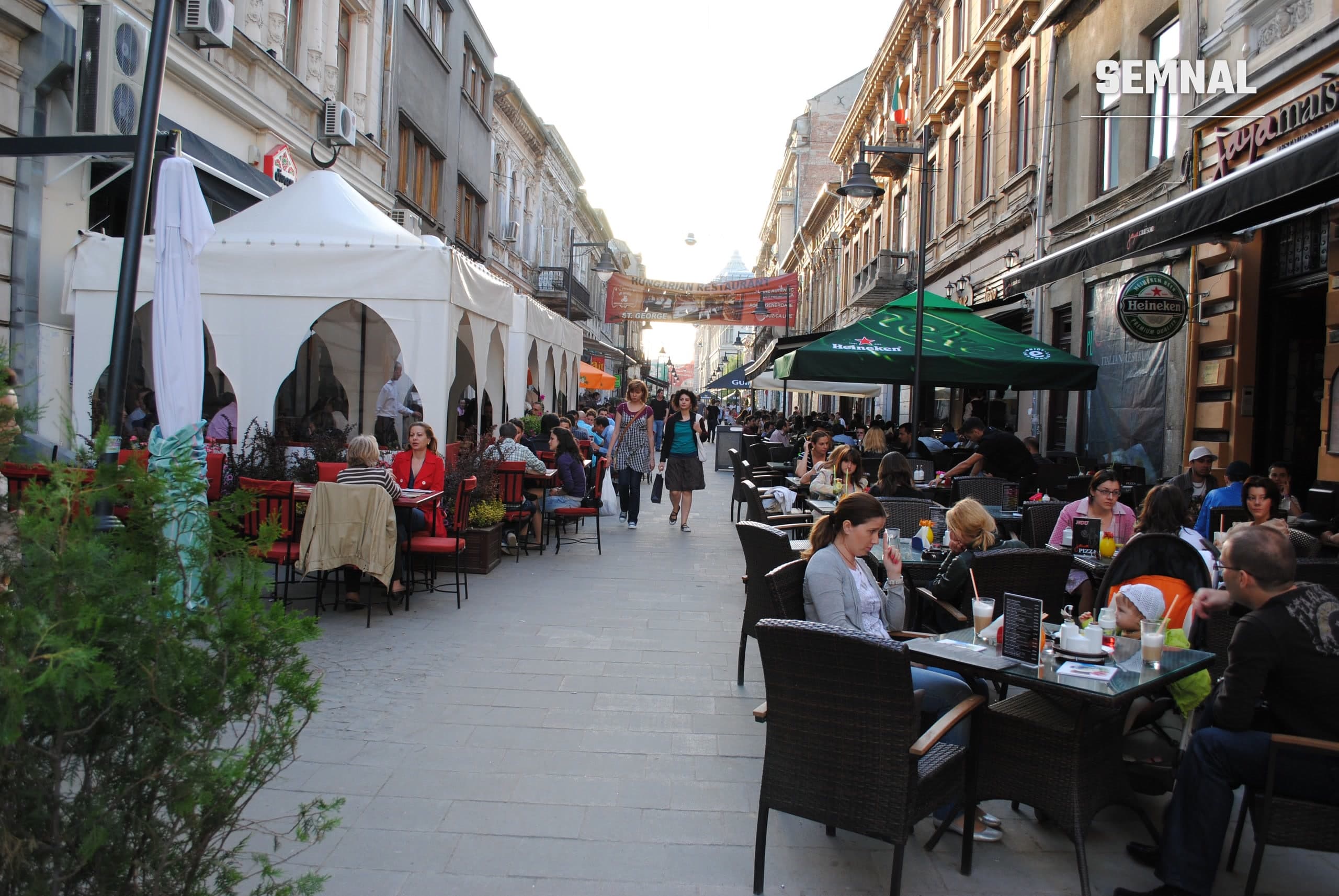 Terase cu mese pe o stradă pietonală din Centrul Vechi al Bucureștiului, cu clădiri istorice pe ambele părți