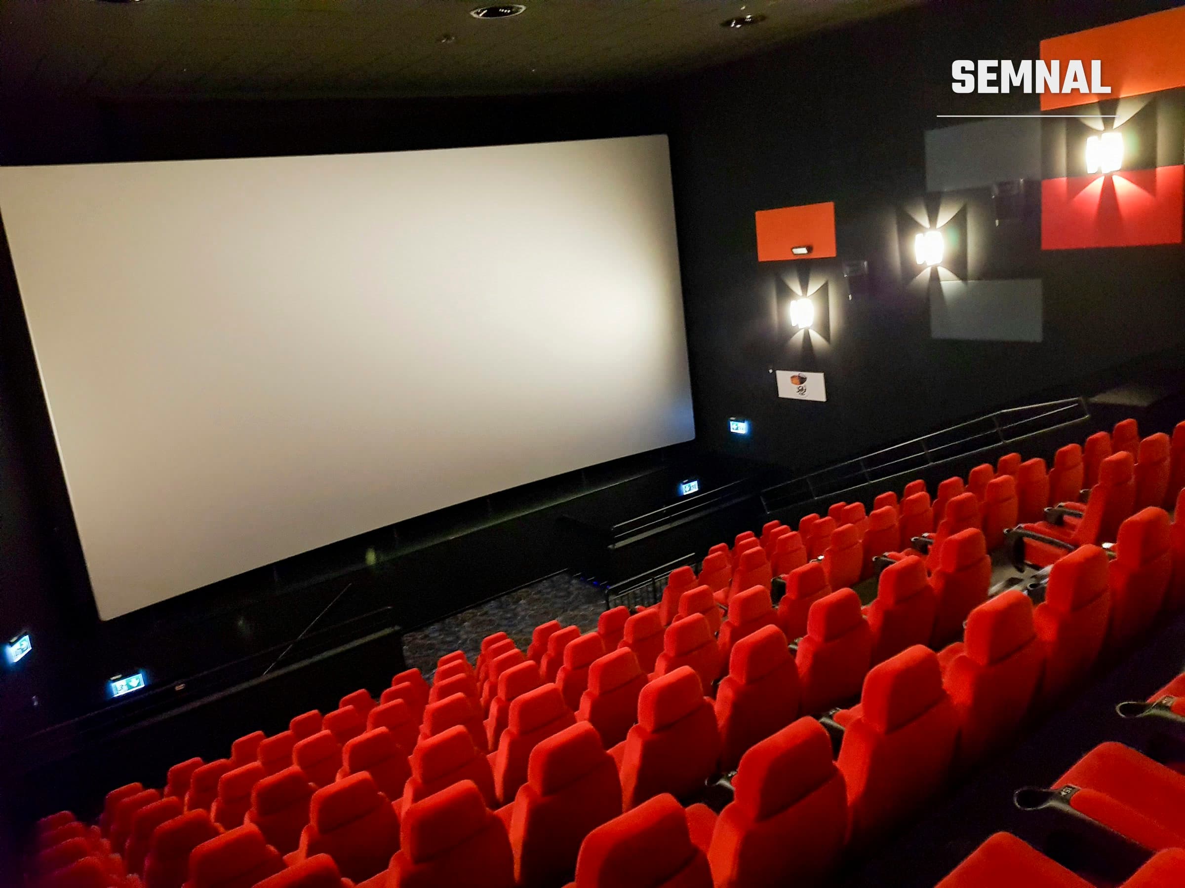Sală de cinema goală, cu scaune roșii și ecran alb, înainte de proiecție