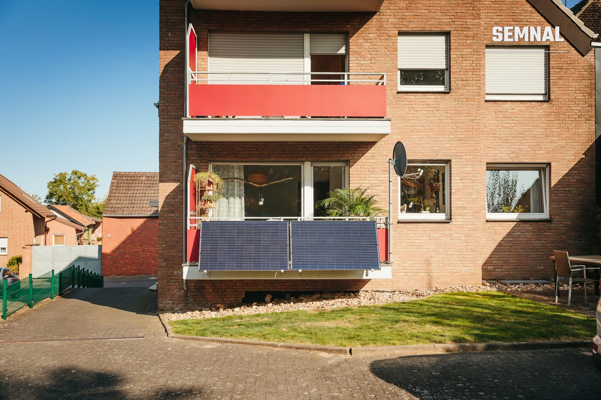 Panouri fotovoltaice de tip balcon montate pe balustrada unui balcon, prinse de fațada de cărămidă a unui bloc