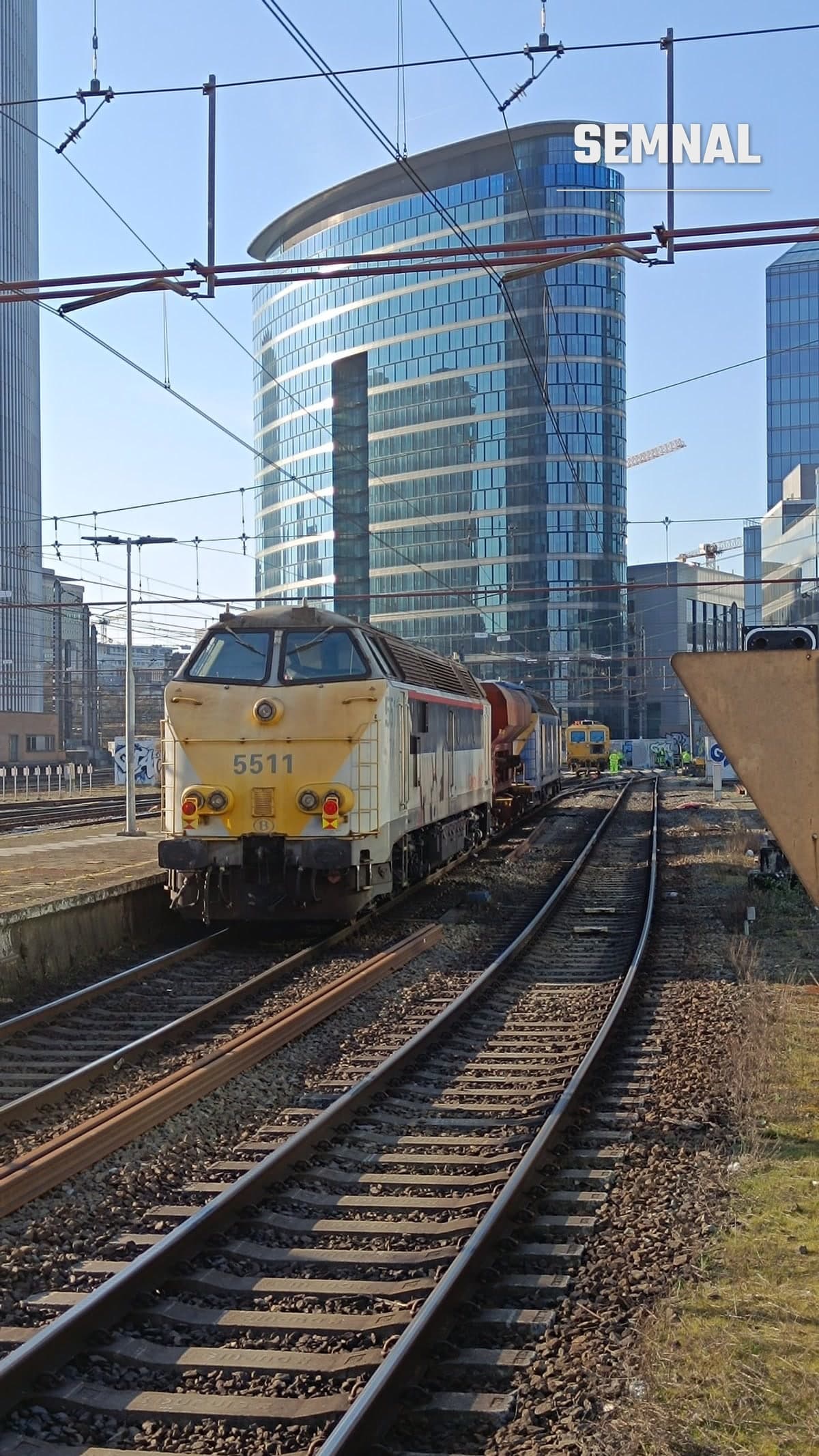 Tren pe calea ferată belgiană, plecare spre Bruges, cu turnuri moderne în fundal