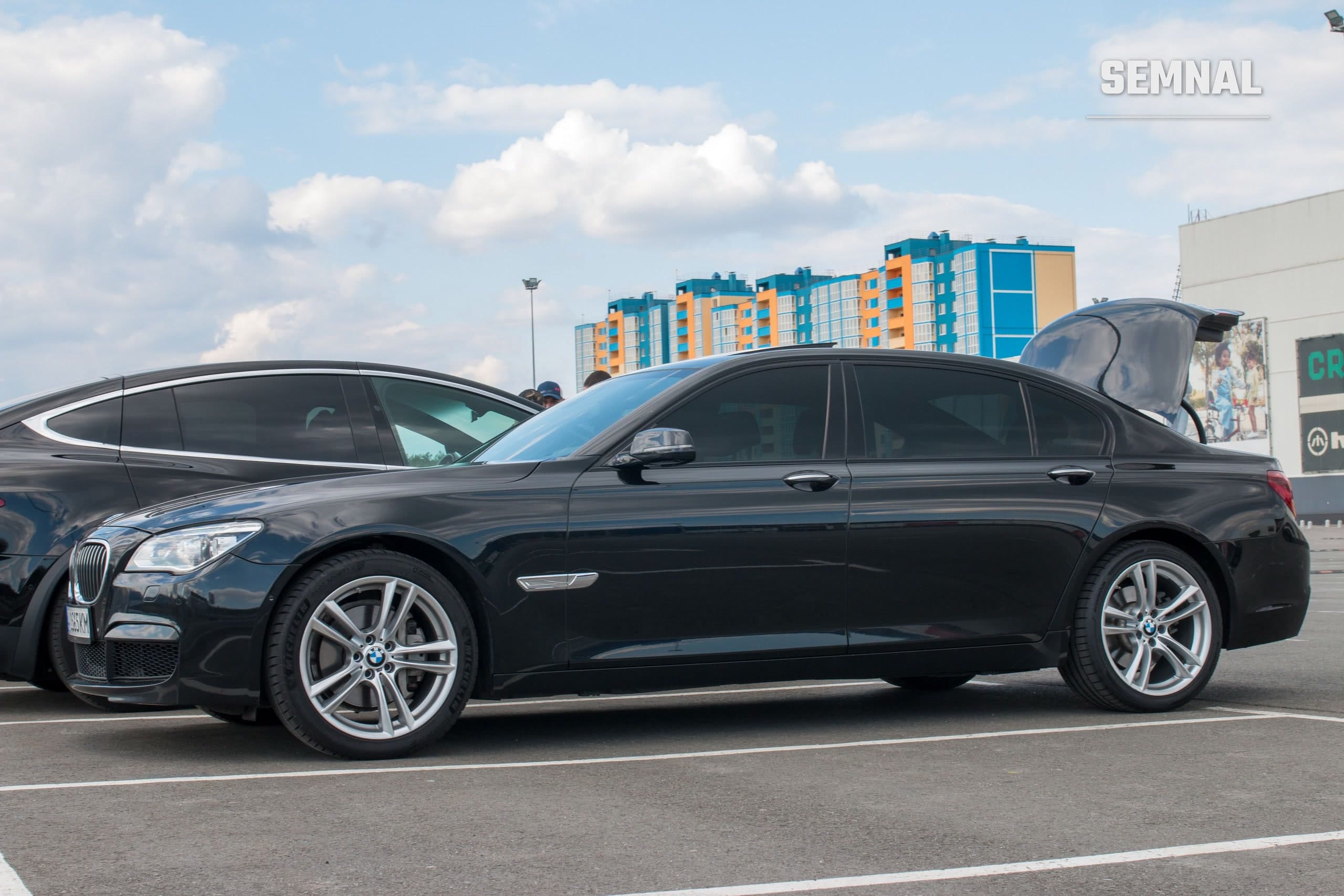 BMW Seria 7, limuzină neagră, văzută din lateral, parcată într-un cadru urban modern