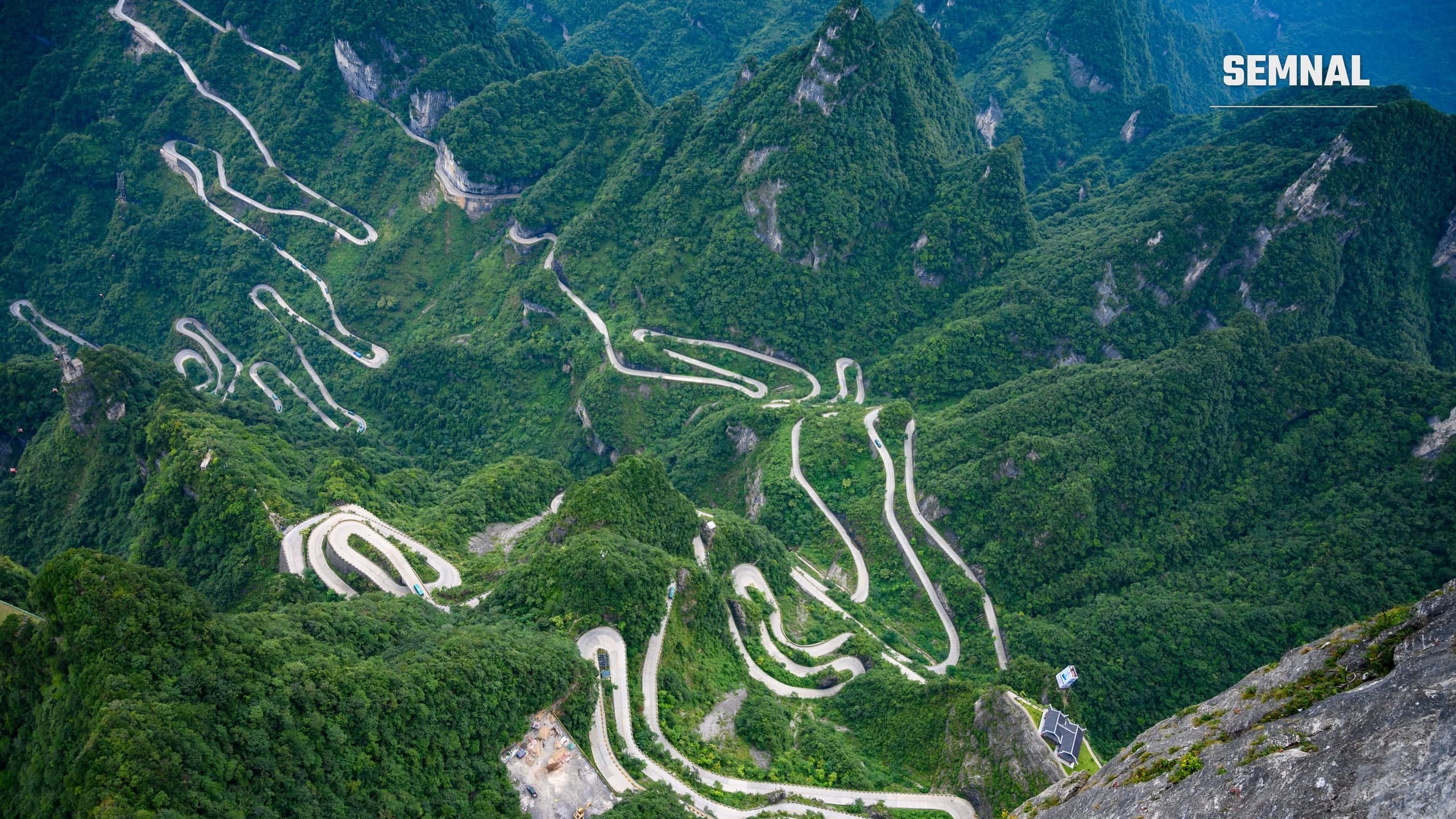 Vedere de sus asupra drumului cu 99 de viraje de pe Muntele Tianmen, în China, șerpuind printre versanți acoperiți de vegetație