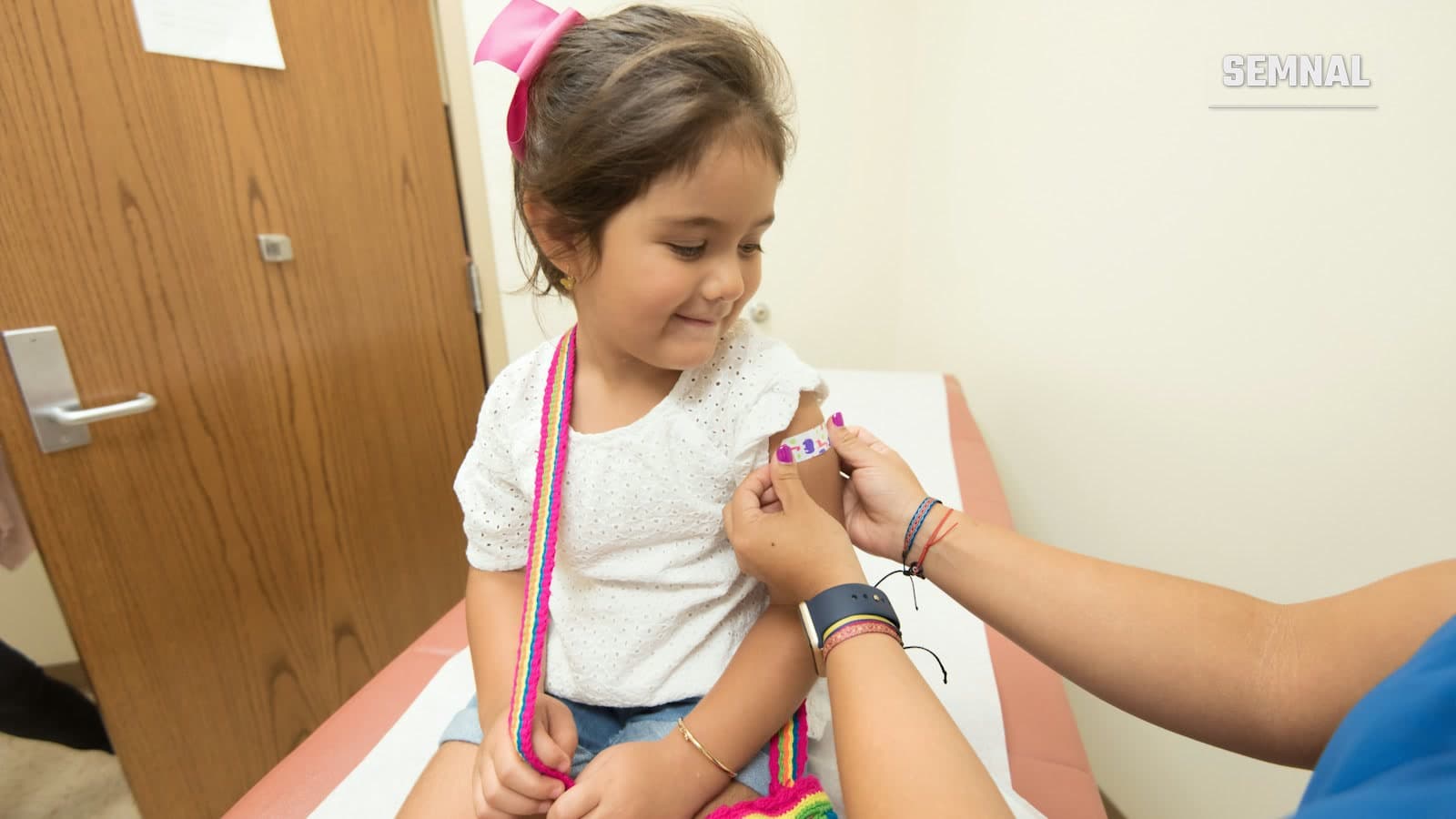 Un cadru medical vaccinează o fetiță în cabinet, în timp ce aceasta privește spre cameră