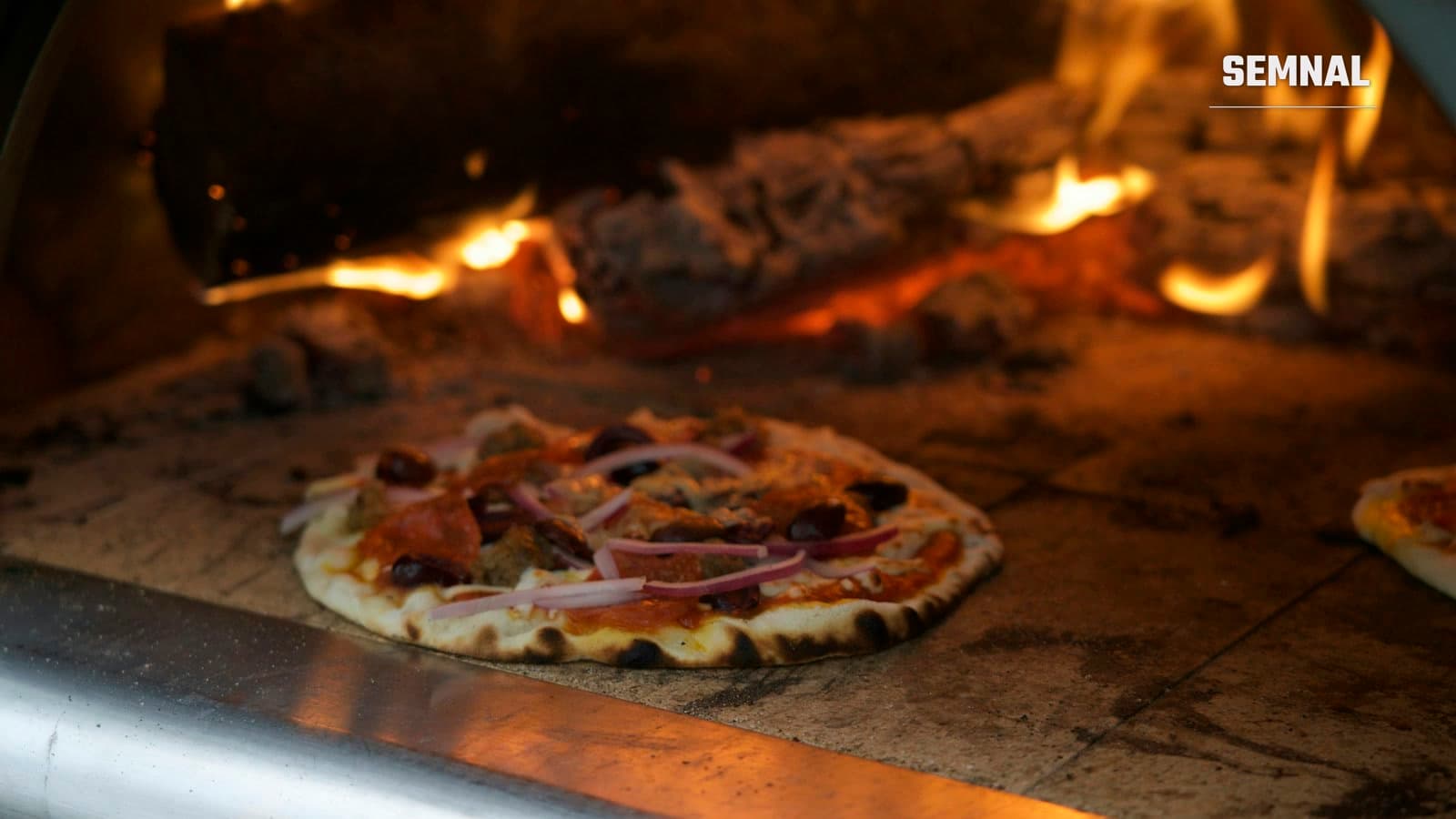 Pizza napoletană gătită într-un cuptor cu lemne, cu flăcările vizibile în fundal