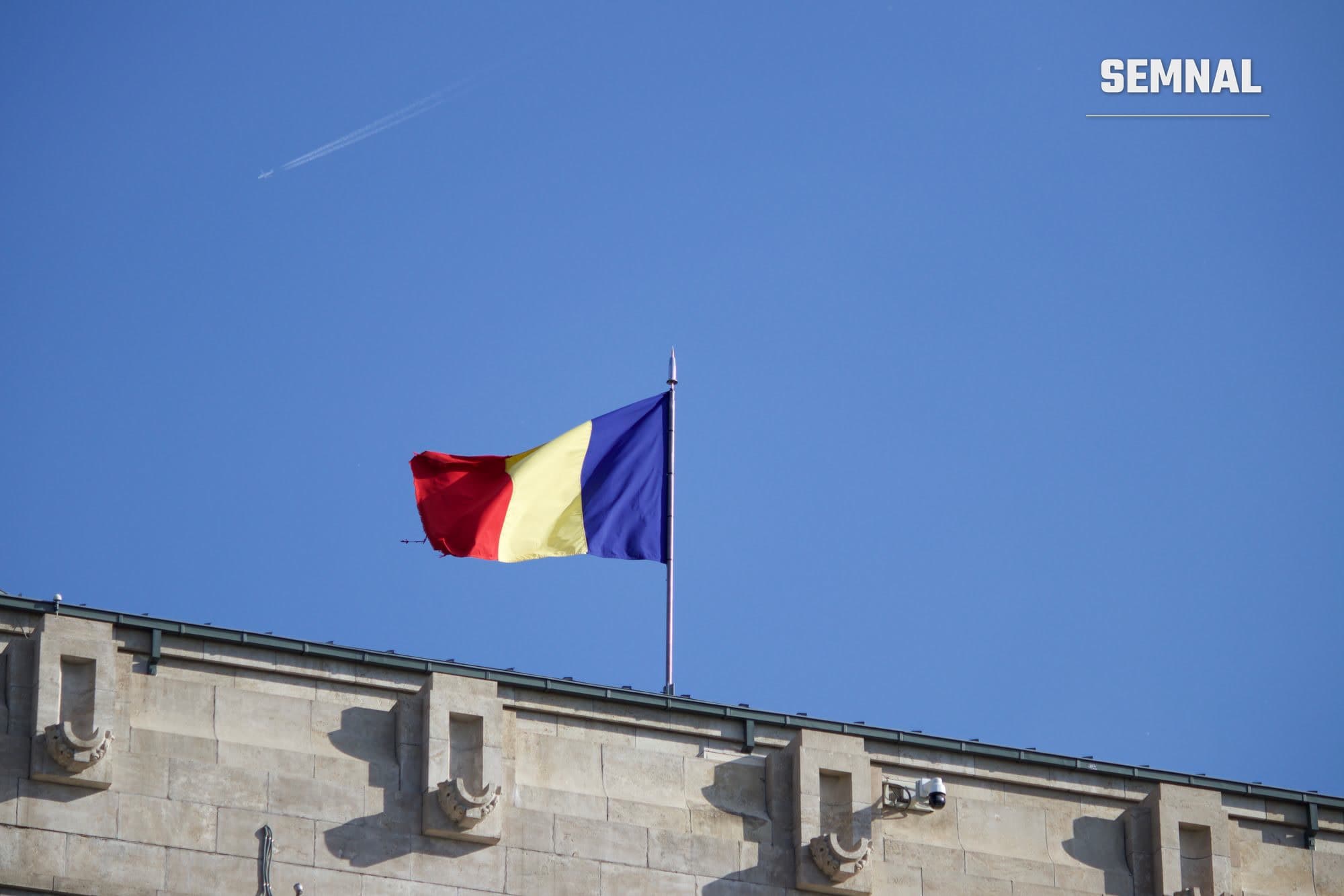 Drapelul României fluturând pe un catarg, sub un cer albastru, la București