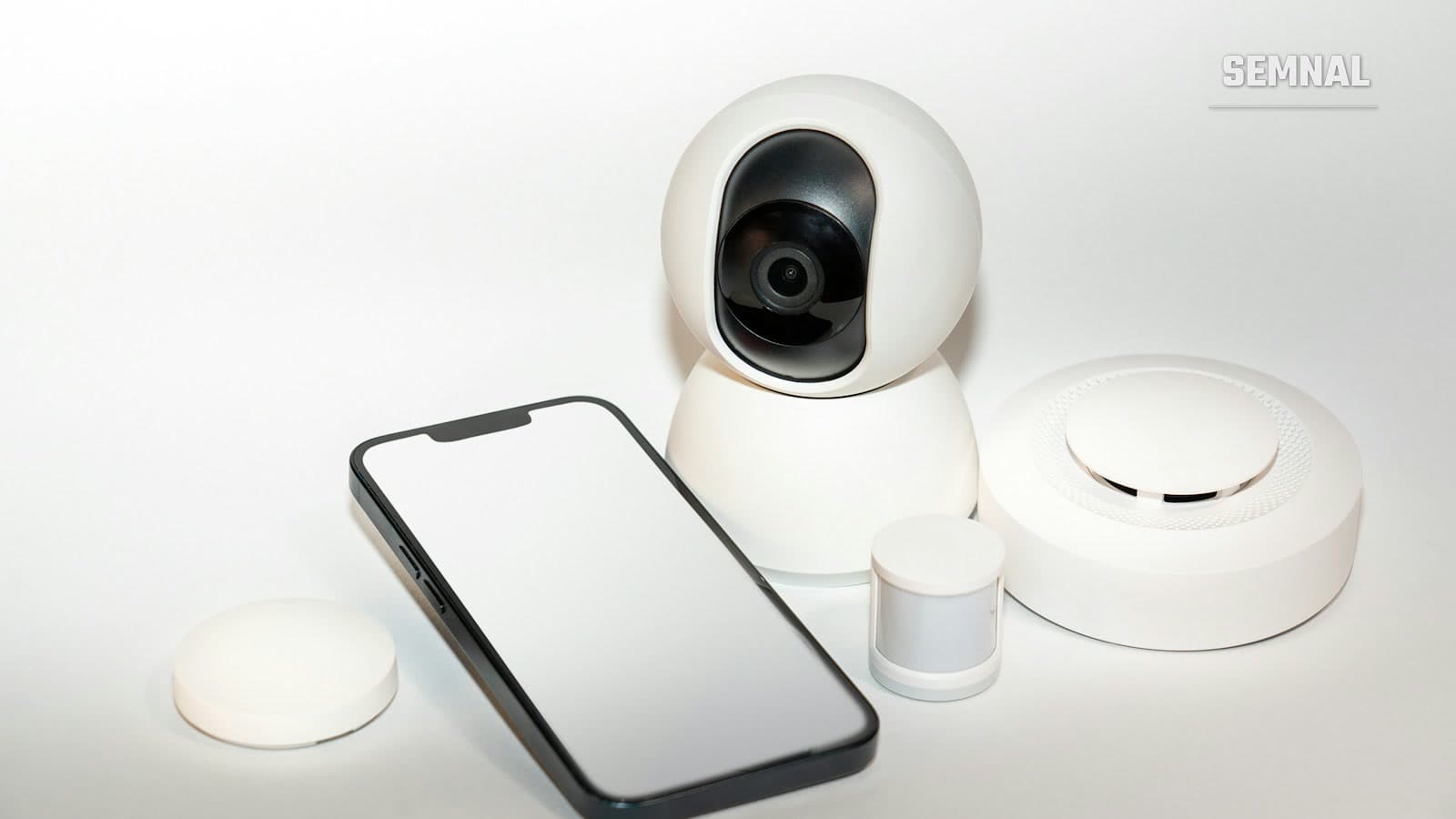 Cameră de supraveghere smart, rotativă, de interior, așezată lângă un smartphone și alți senzori pentru casă inteligentă