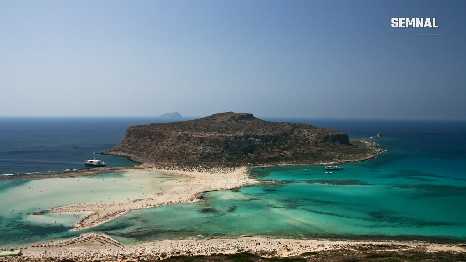 Vedere de pe o stâncă spre o mică insulă înconjurată de apa turcoaz a mării, pe coasta Cretei, în Grecia