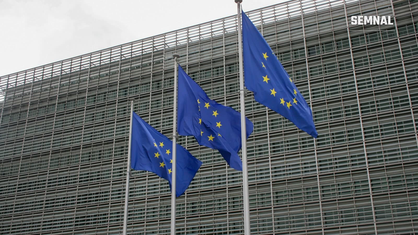 Trei steaguri ale Uniunii Europene fluturând în fața unei clădiri instituționale la Bruxelles