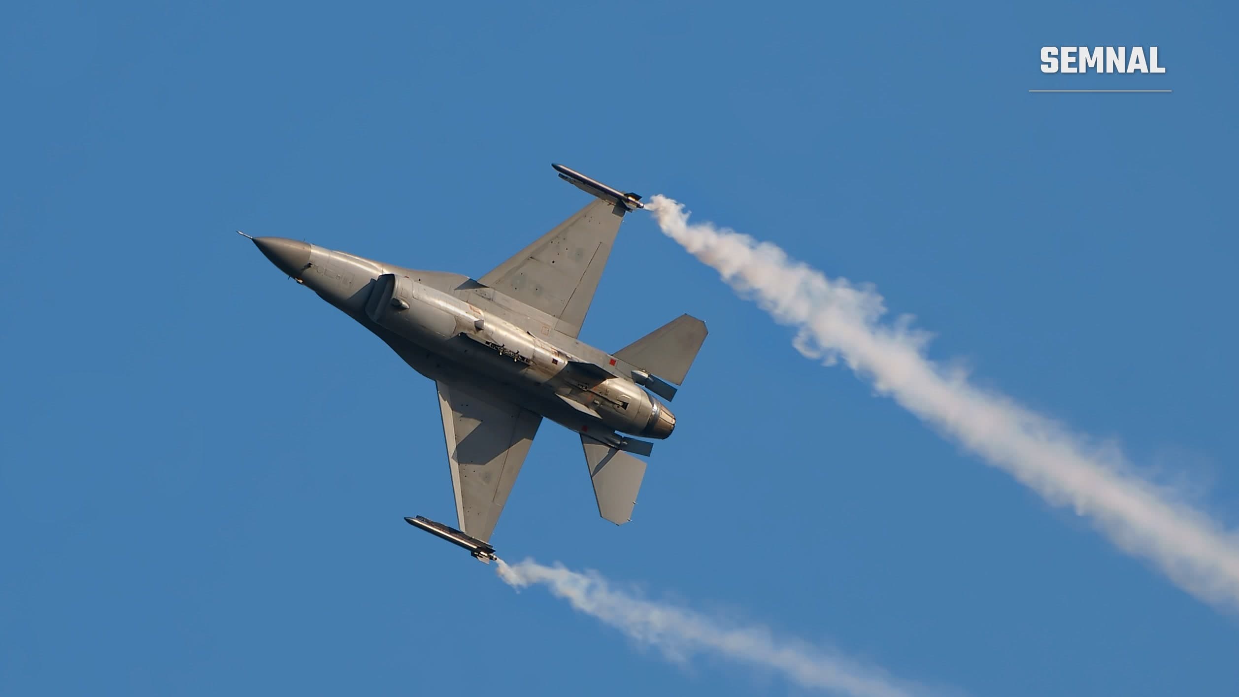 Avion de vânătoare F-16 al forțelor aeriene belgiene, văzut de jos în zbor, cu dâre de fum pe un cer albastru