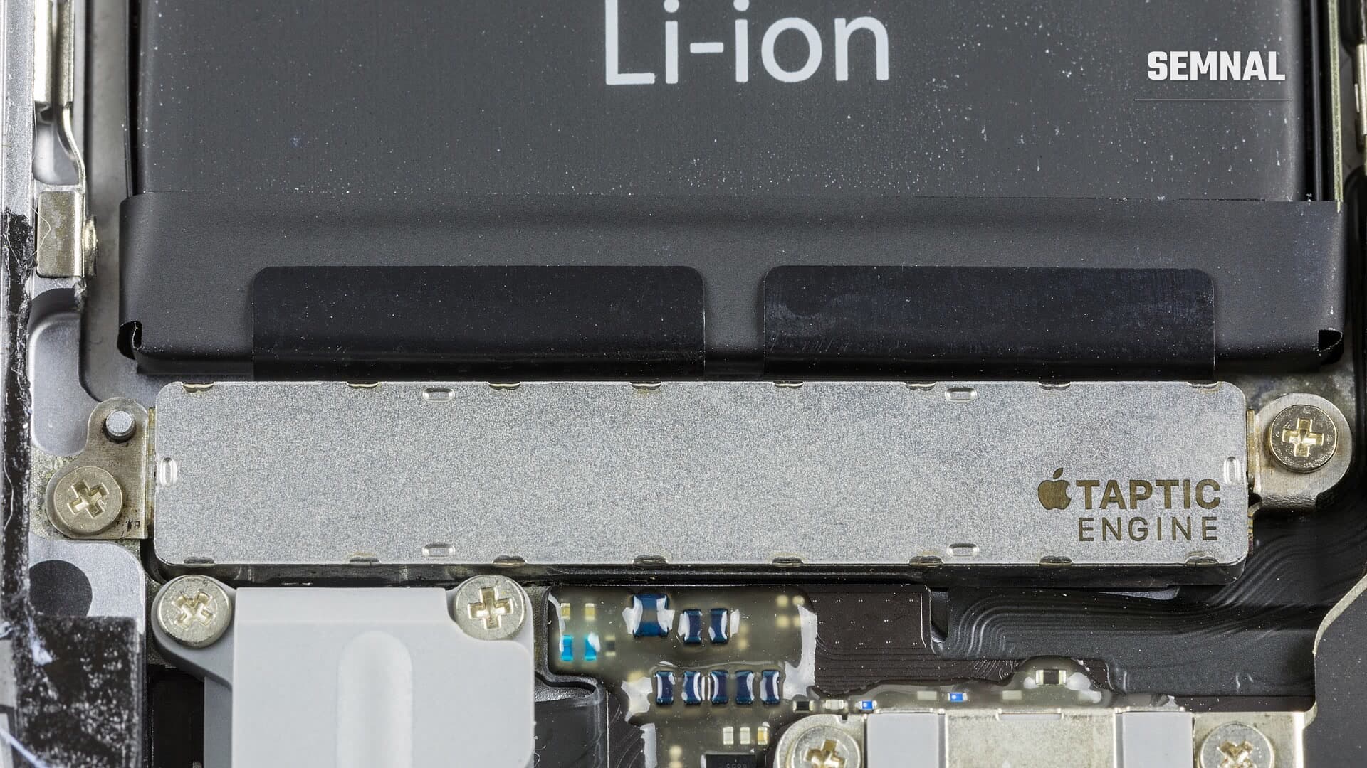 Taptic Engine, modulul de vibrații al unui iPhone 6s demontat, vizibil sub baterie, cu inscripția producătorului pe carcasa metalică