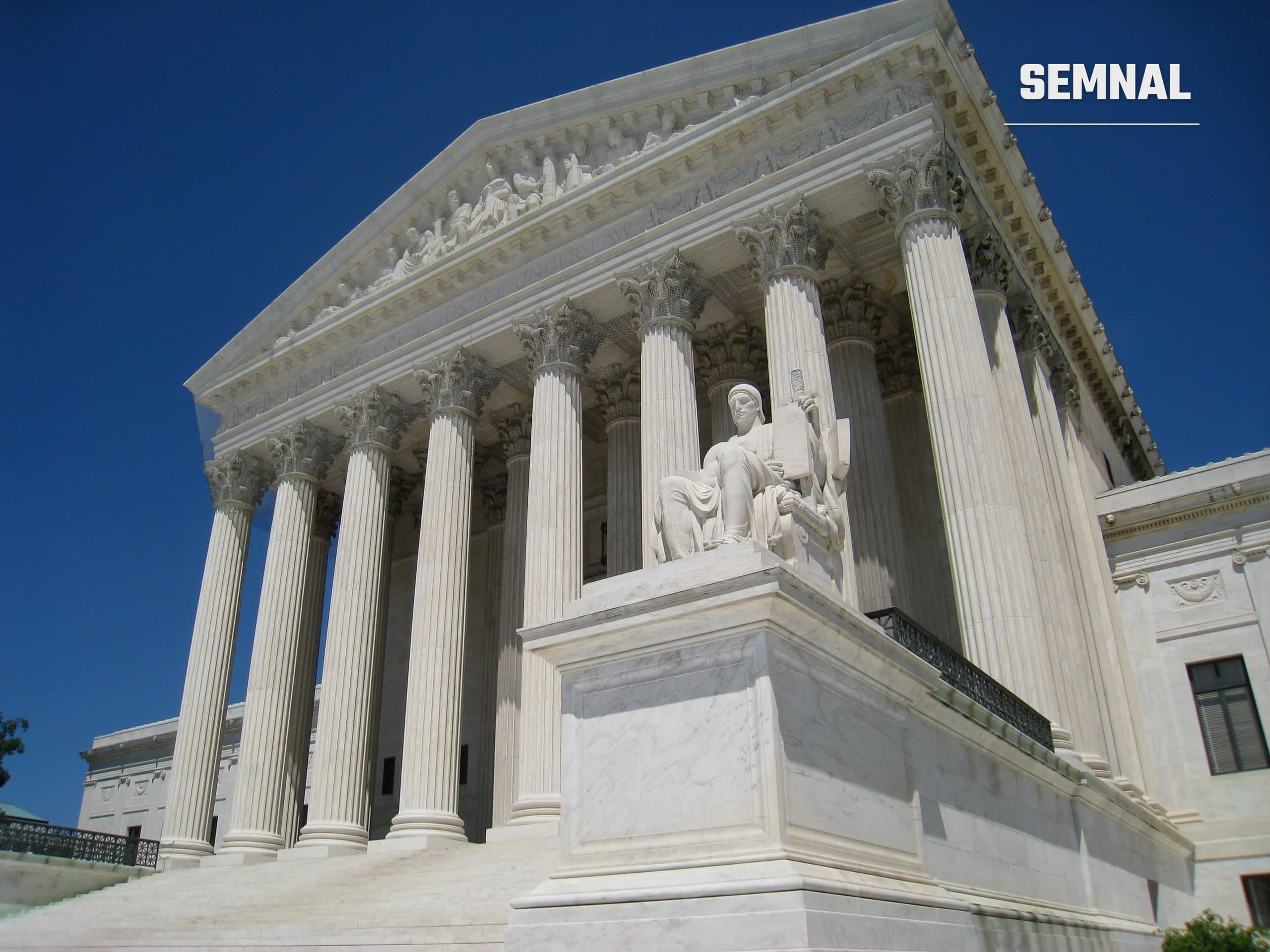 Fațada de marmură a clădirii Curții Supreme a SUA din Washington, cu coloane înalte și o statuie așezată în fața intrării, sub cer senin