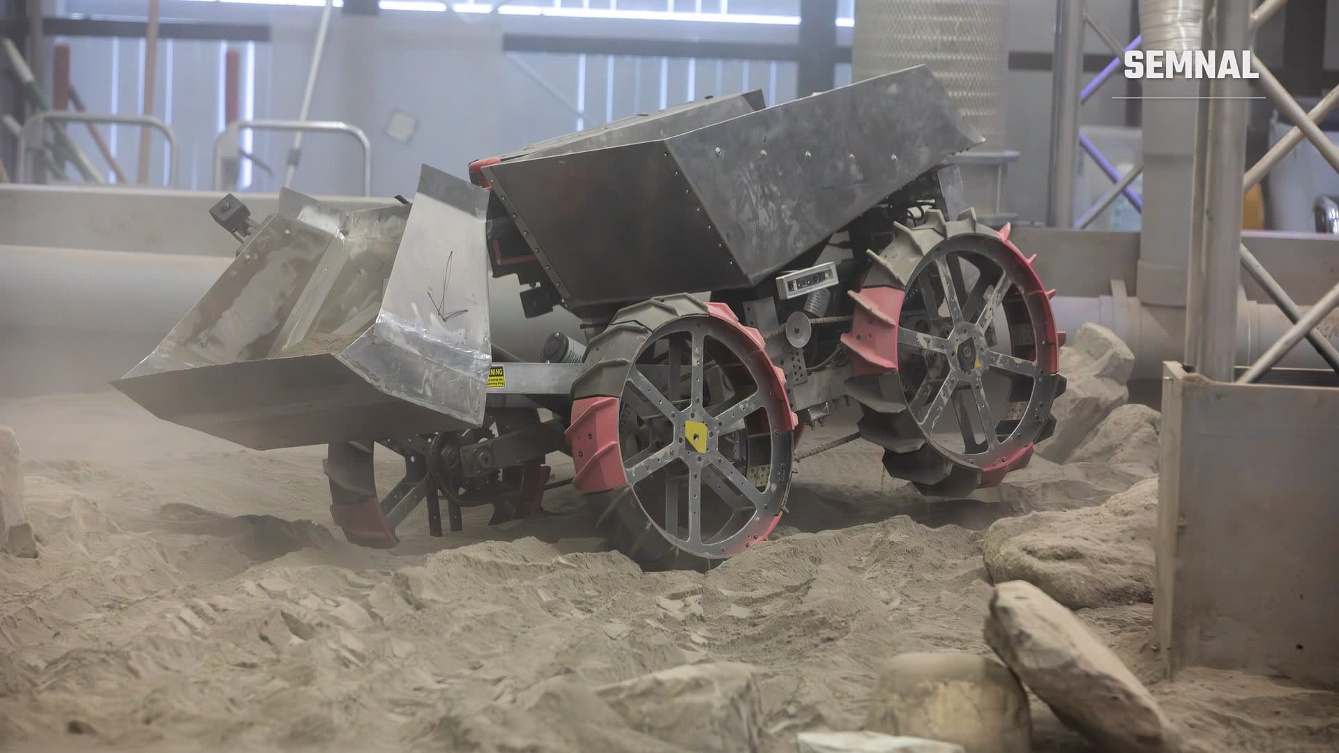 Rover cu cupă de excavare și roți late, pe regolit simulat printre pietre, la finala NASA Lunabotics din mai 2026, în Florida