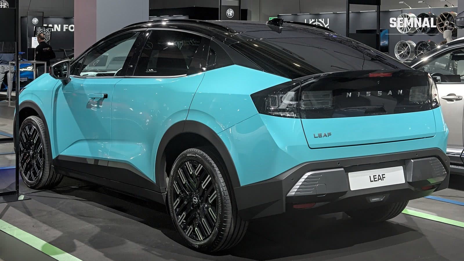 Nissan Leaf de a treia generație, turcoaz cu plafon negru, văzut din spate și lateral, expus pe un stand la un salon auto