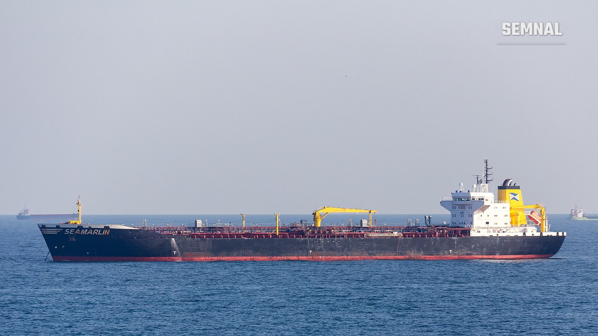 Petrolierul Seamarlin, cu corpul negru și suprastructura albă cu galben, ancorat pe o mare calmă, sub un cer cețos. Foto: Raimond Spekking / Wikimedia Commons, CC BY-SA 4.0