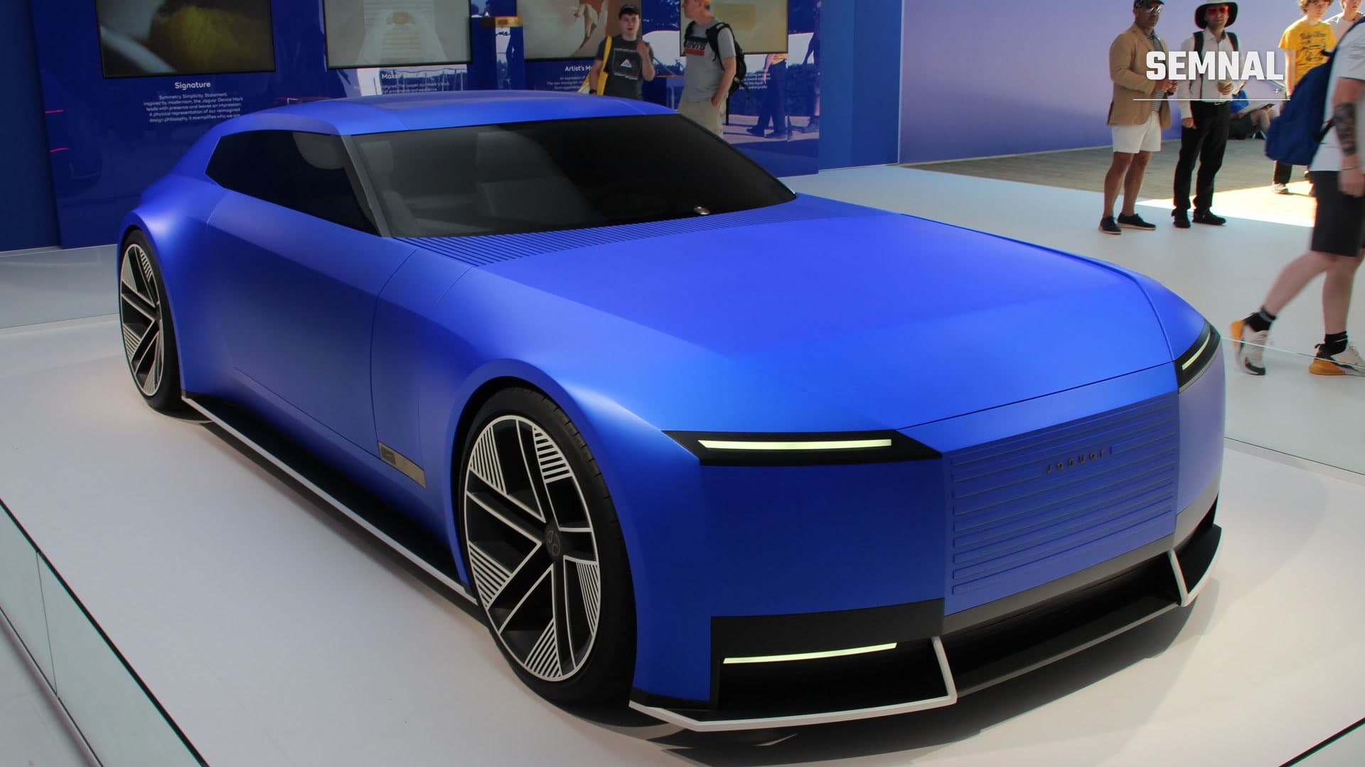 Conceptul Jaguar Type 00, precursorul modelului Type 01, în albastru mat, văzut din față și din lateral pe un podium de expoziție, cu vizitatori în fundal