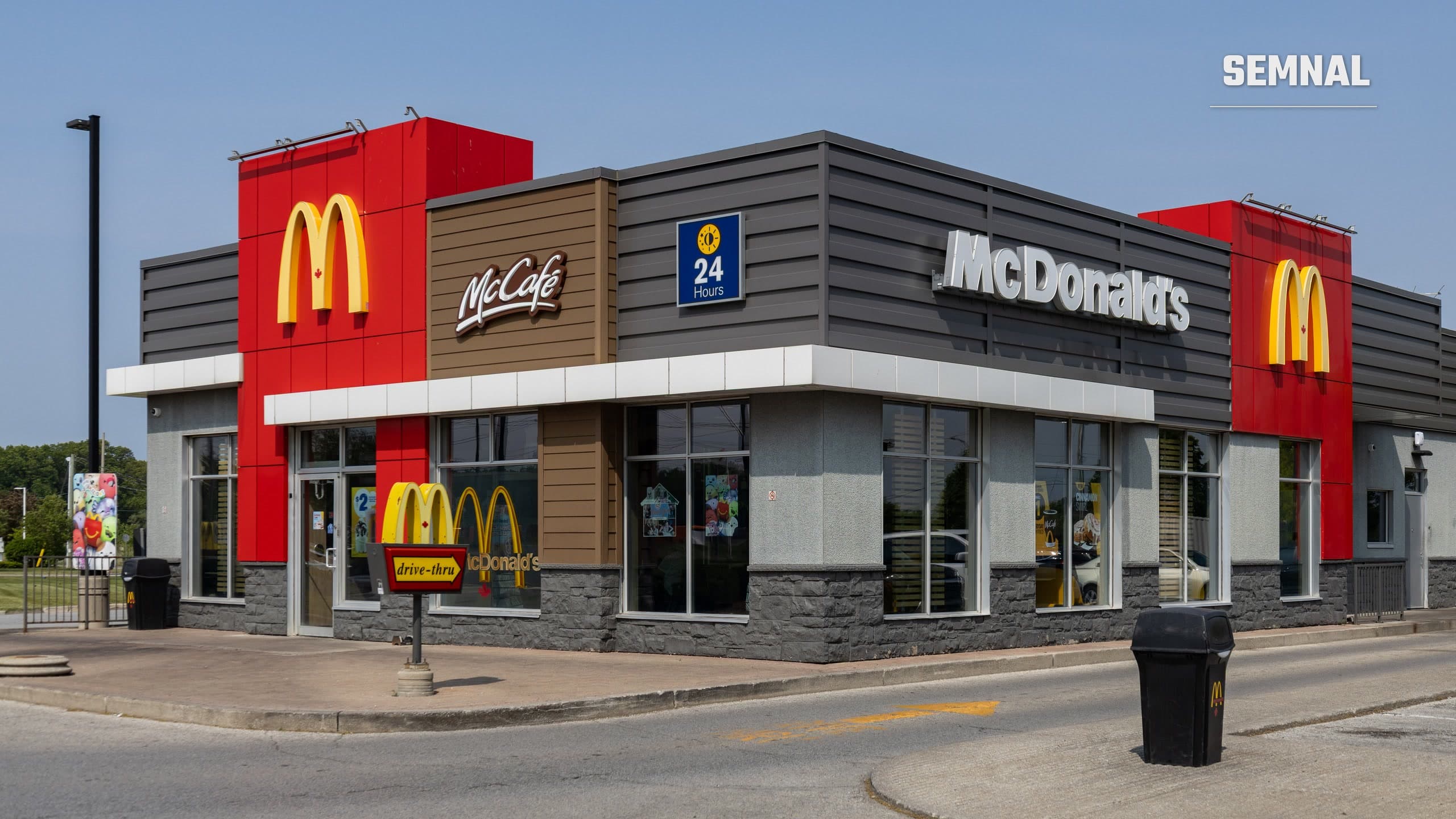 Restaurant McDonald's cu fațadă roșie și gri, arcade aurii și indicator de drive-thru, fotografiat într-o zi senină la Windsor, Ontario