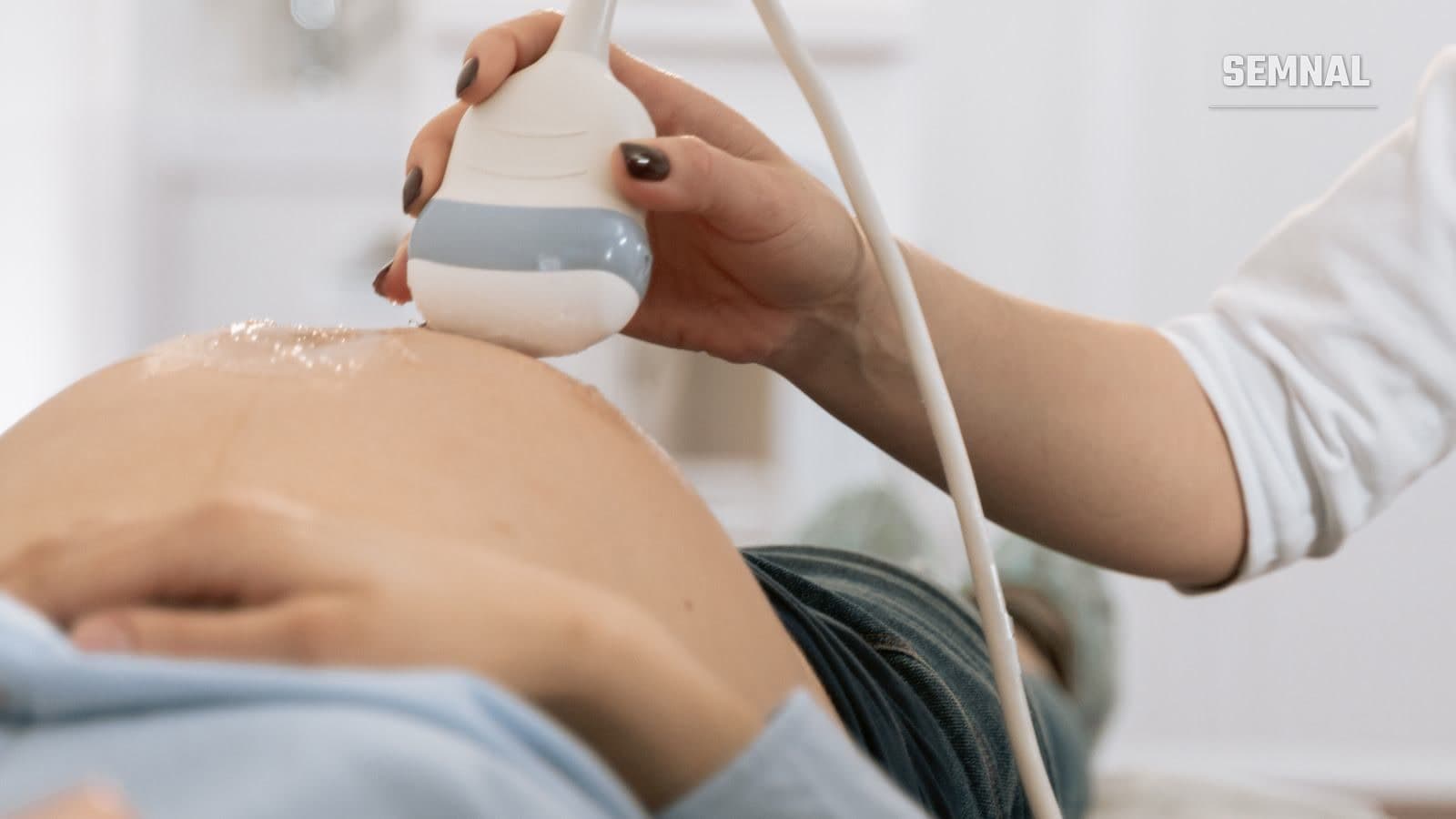 Medic ținând o sondă ecografică pe abdomenul unei femei însărcinate, în timpul unei ecografii