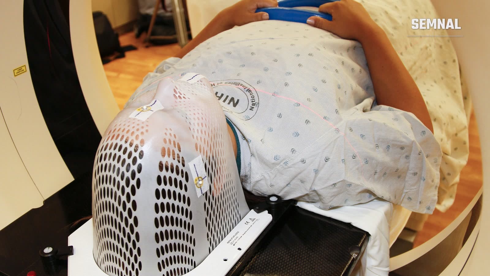 Model așezat într-un aparat de tomografie computerizată, cu o mască de imobilizare perforată pe cap, pregătit pentru imagistica dinaintea unei radioterapii