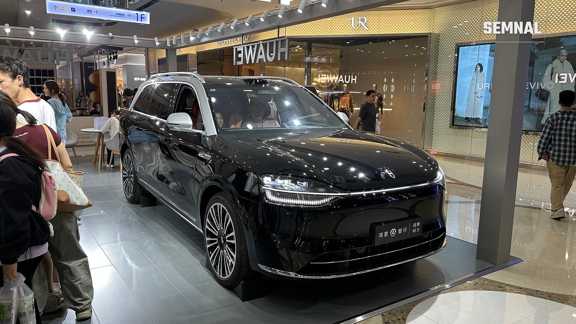 SUV-ul electric Aito M9 negru, expus într-un spațiu comercial Huawei dintr-un mall, cu vizitatori în jur