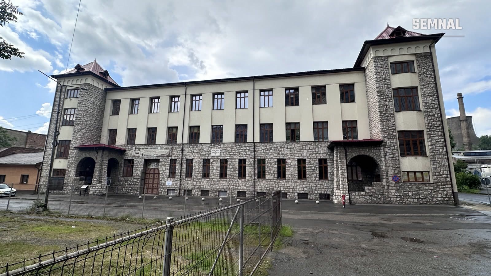 Clădirea principală a Colegiului Național Diaconovici-Tietz din Reșița, cu fațadă de piatră, două turnuri și coșul istoric de fum în fundal