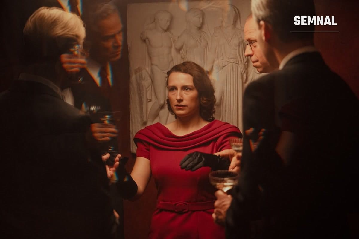 Cadru din filmul Woman Unknown, câștigătorul Leului de Aur la Veneția, cu o femeie în rochie roșie într-un grup de bărbați