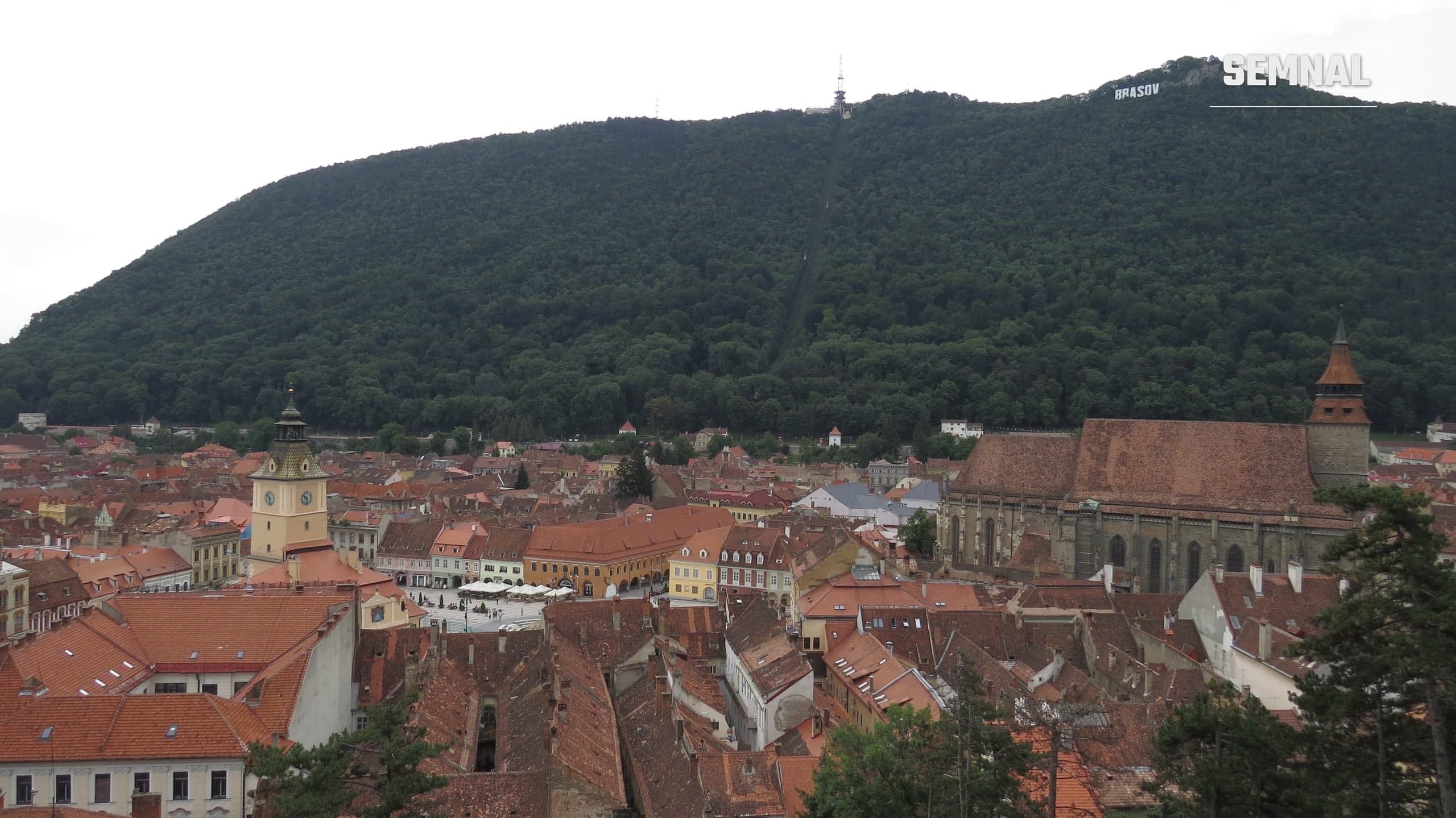 Panoramă a centrului istoric al Brașovului, cu Biserica Neagră și turnul Casei Sfatului, iar în fundal dealul Tâmpa acoperit de pădure