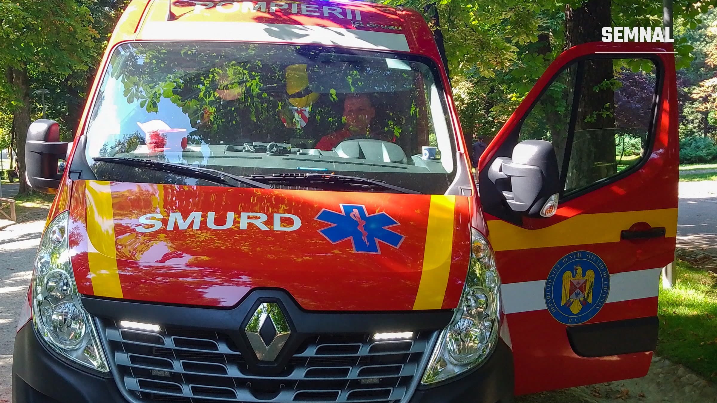 Ambulanță SMURD văzută din față, într-un parc, cu ușa din dreapta deschisă și însemnele serviciului pe capotă, imagine ilustrativă. (Foto: Spotting the World / Wikimedia Commons, CC BY-SA 4.0)