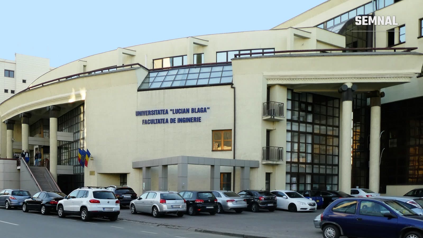 Clădirea Facultății de Inginerie a Universității „Lucian Blaga” din Sibiu, cu intrare cu coloane, steaguri și mașini parcate în față