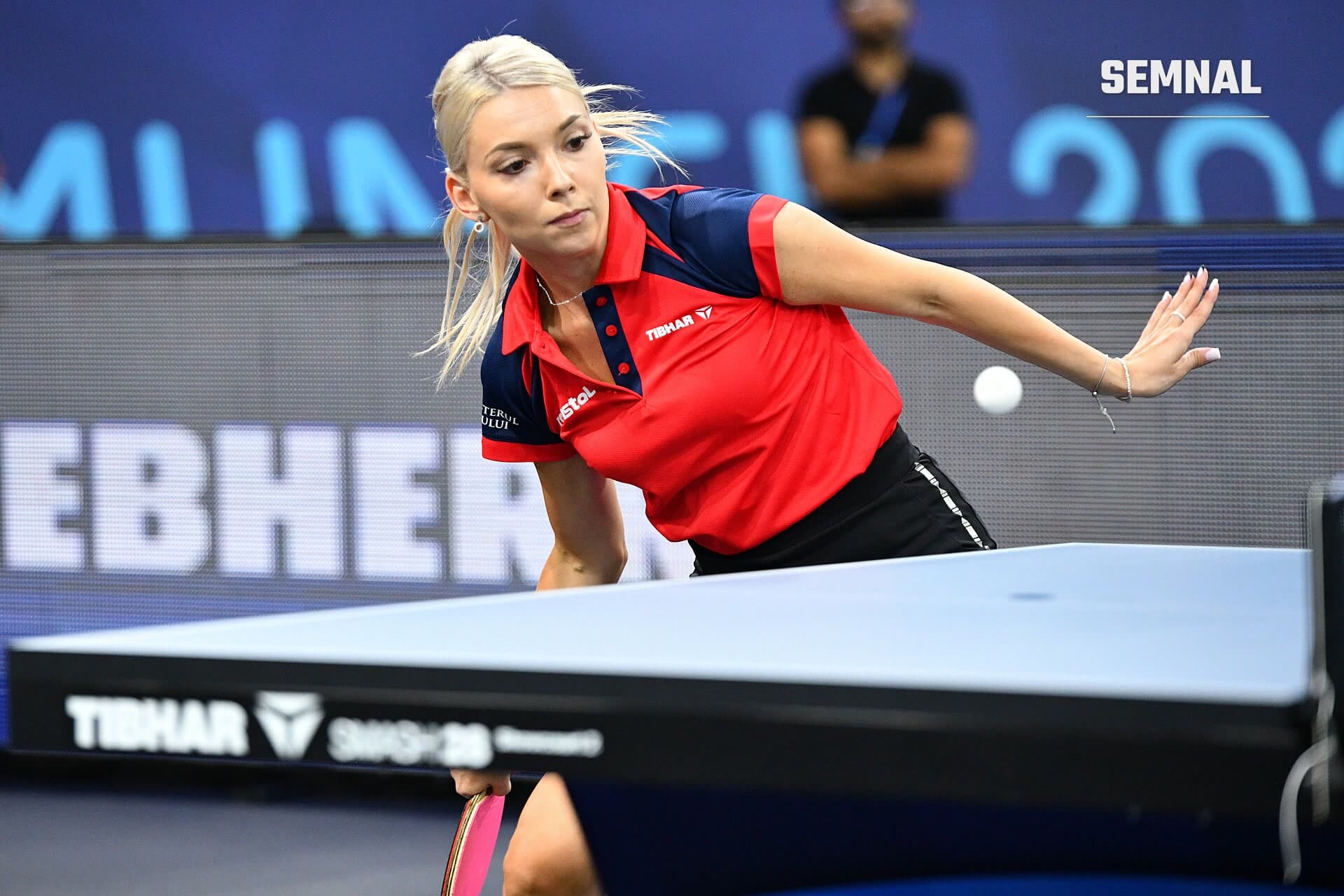 Bernadette Szocs, în tricou roșu, returnează mingea la masă în timpul unui meci la Campionatele Europene din 2022, de la München