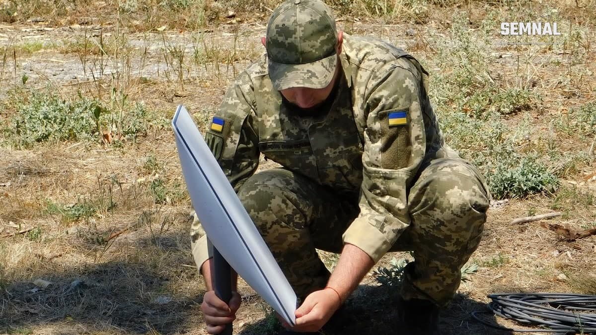 Militar ucrainean în uniformă de camuflaj instalează o antenă de satelit Starlink pe un teren cu iarbă uscată. (Foto: Support Forces of Ukraine Command / Wikimedia Commons, CC BY 4.0)