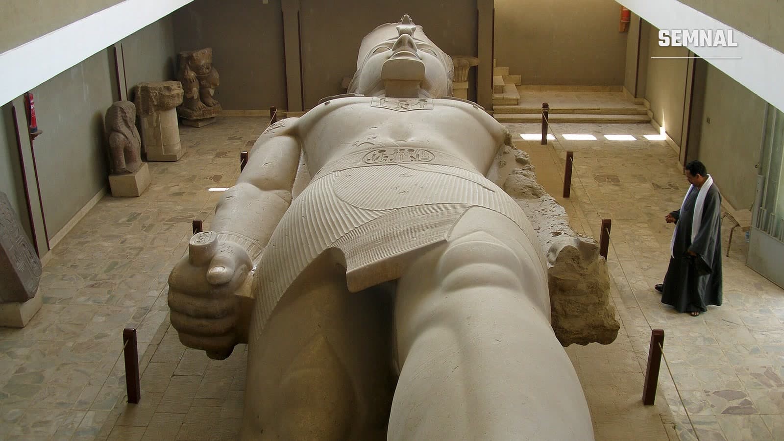 Colosul lui Ramses al II-lea de la Memphis, o statuie uriașă din calcar întinsă pe spate într-o sală de muzeu, văzută de sus