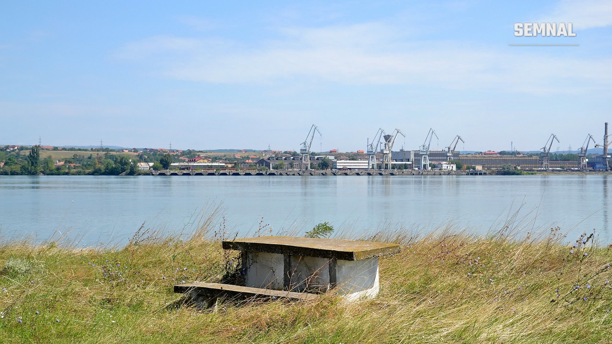 Malul românesc al Dunării la Drobeta-Turnu Severin, cu macarale industriale, văzut peste apă dinspre fortăreața Kladovo din Serbia