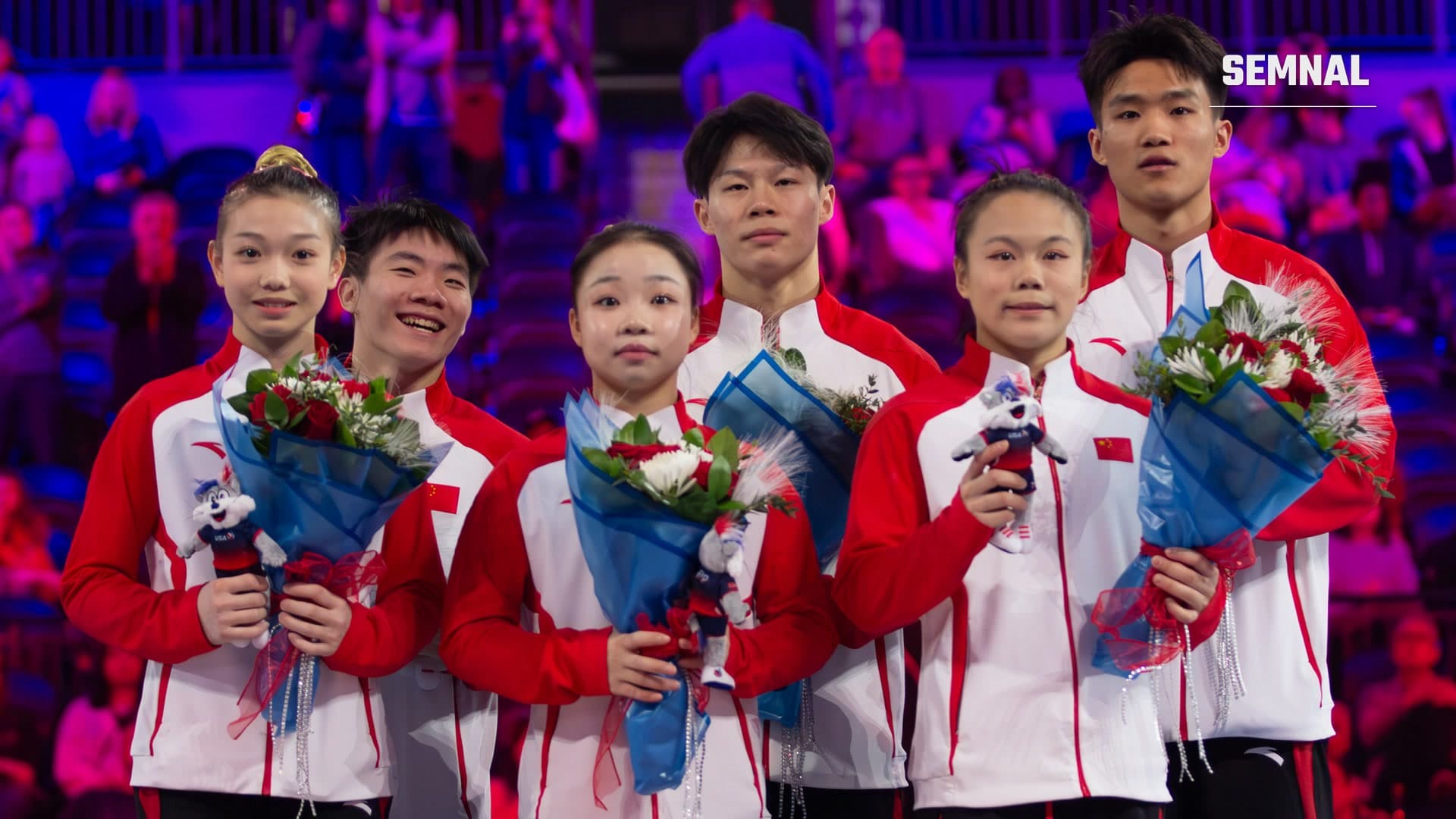 Gimnaștii echipei naționale a Chinei, în uniforme roșu cu alb, ținând buchete de flori și mascote, pe podium la American Cup 2026
