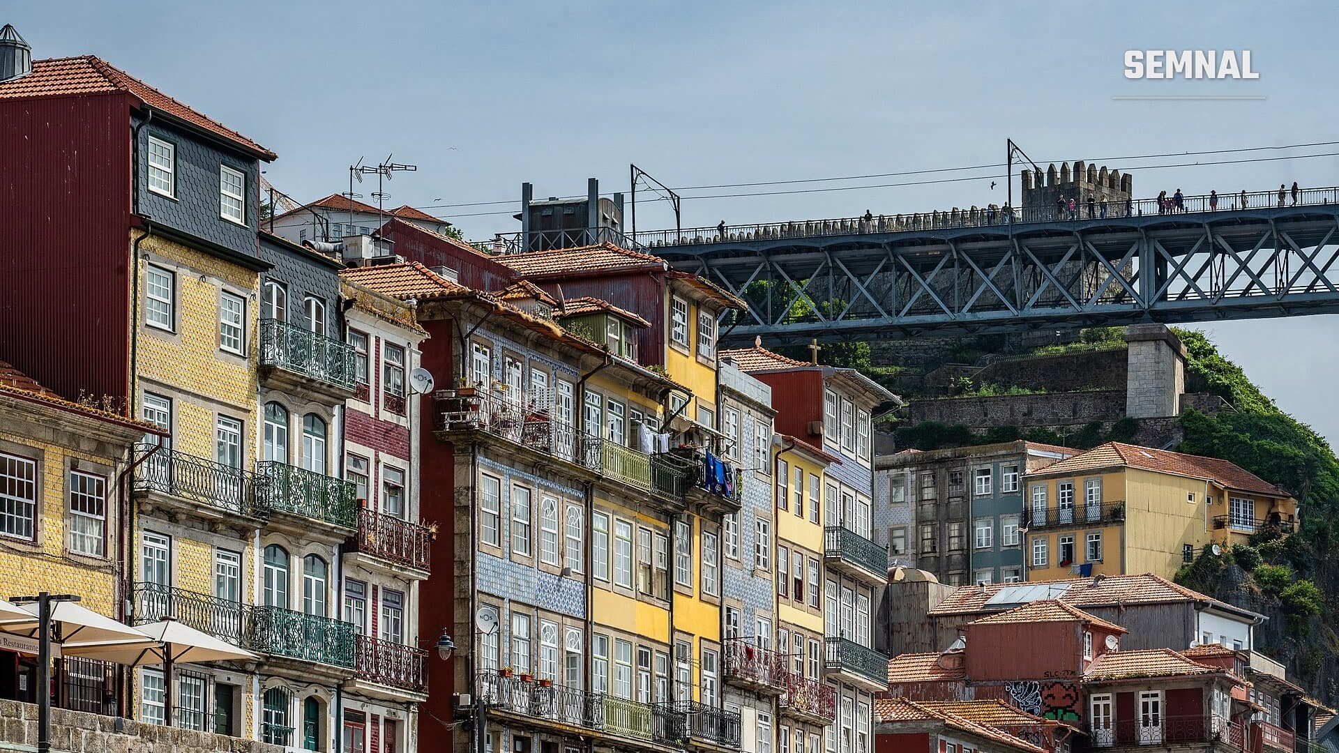 Clădiri colorate cu fațade din plăci de faianță și balcoane din fier forjat în cartierul Ribeira din Porto, iar în planul din spate se vede podul Dom Luís I