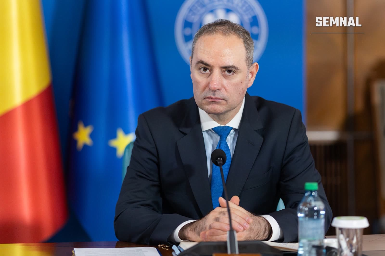 Ministrul Finanțelor, Alexandru Nazare, la o masă de ședință, în fața drapelelor României și Uniunii Europene