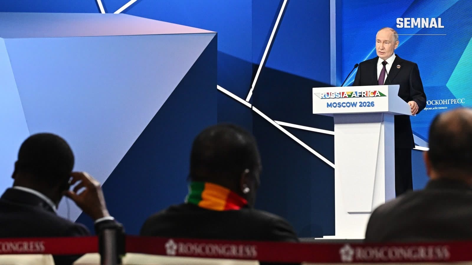 Vladimir Putin vorbește la tribuna cu inscripția Russia-Africa Moscow 2026, privit din sală de delegați africani, la Forumul economic și umanitar Rusia-Africa