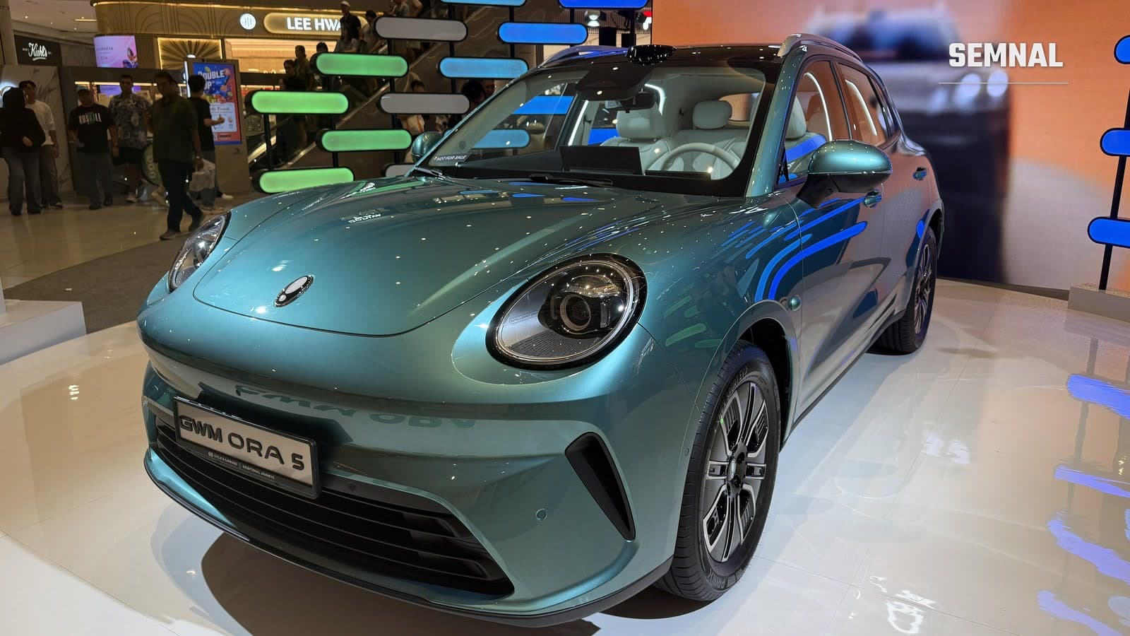 SUV-ul electric compact GWM Ora 5, de culoare verde-turcoaz, expus pe un podium alb la Singapore Motor Show, văzut din față și din lateral