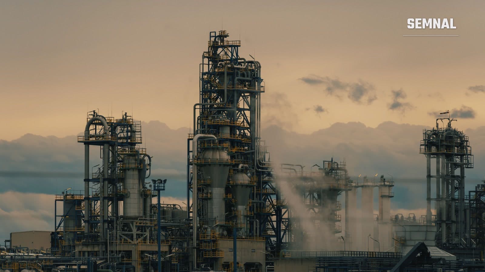 Instalații de rafinare a petrolului la amurg: turnuri metalice cu platforme și conducte, aburi care se ridică pe fundalul unui cer portocaliu cu nori. Imagine ilustrativă, nu de la rafinăria Petrobrazi.