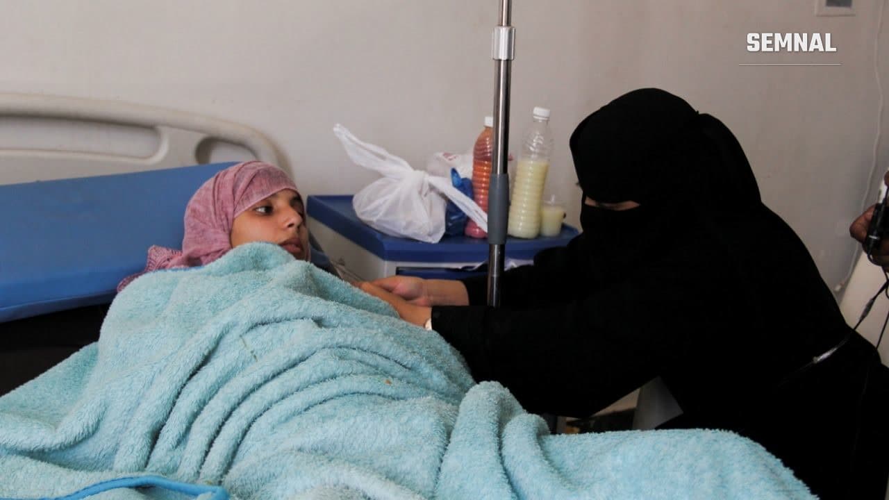 O femeie rănită stă întinsă sub o pătură într-un pat de spital din Taiz, Yemen, în timp ce o rudă îmbrăcată în negru o îngrijește. Foto: Reuters / Anees Mahyoub