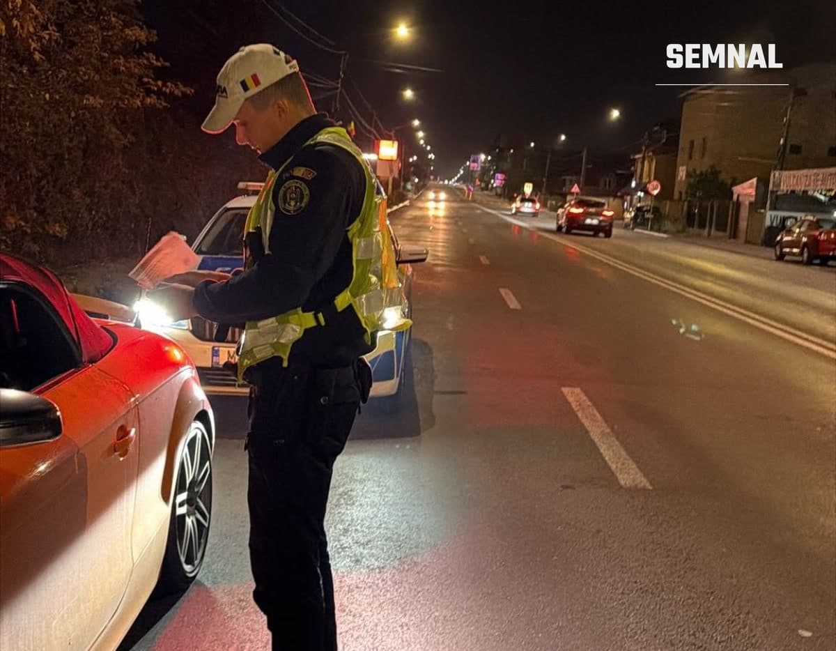 Polițist rutier în vestă reflectorizantă verifică documentele unui șofer, noaptea, pe un drum luminat de stâlpi de iluminat