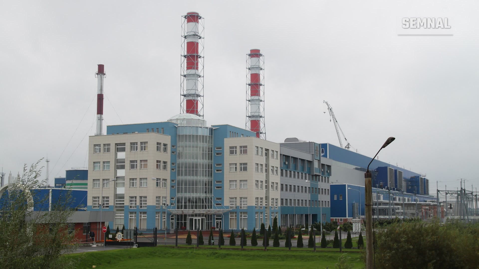 Centrala termoelectrică CET-2 din Kaliningrad, cu două coșuri înalte în dungi roșii și albe și clădiri administrative albastre, pe un cer înnorat