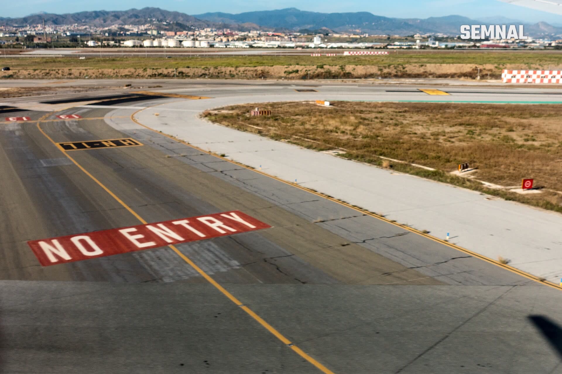 Marcaj roșu „NO ENTRY” pe asfaltul aeroportului din Málaga-Costa del Sol, cu pista, câmpul și dealurile din fundal