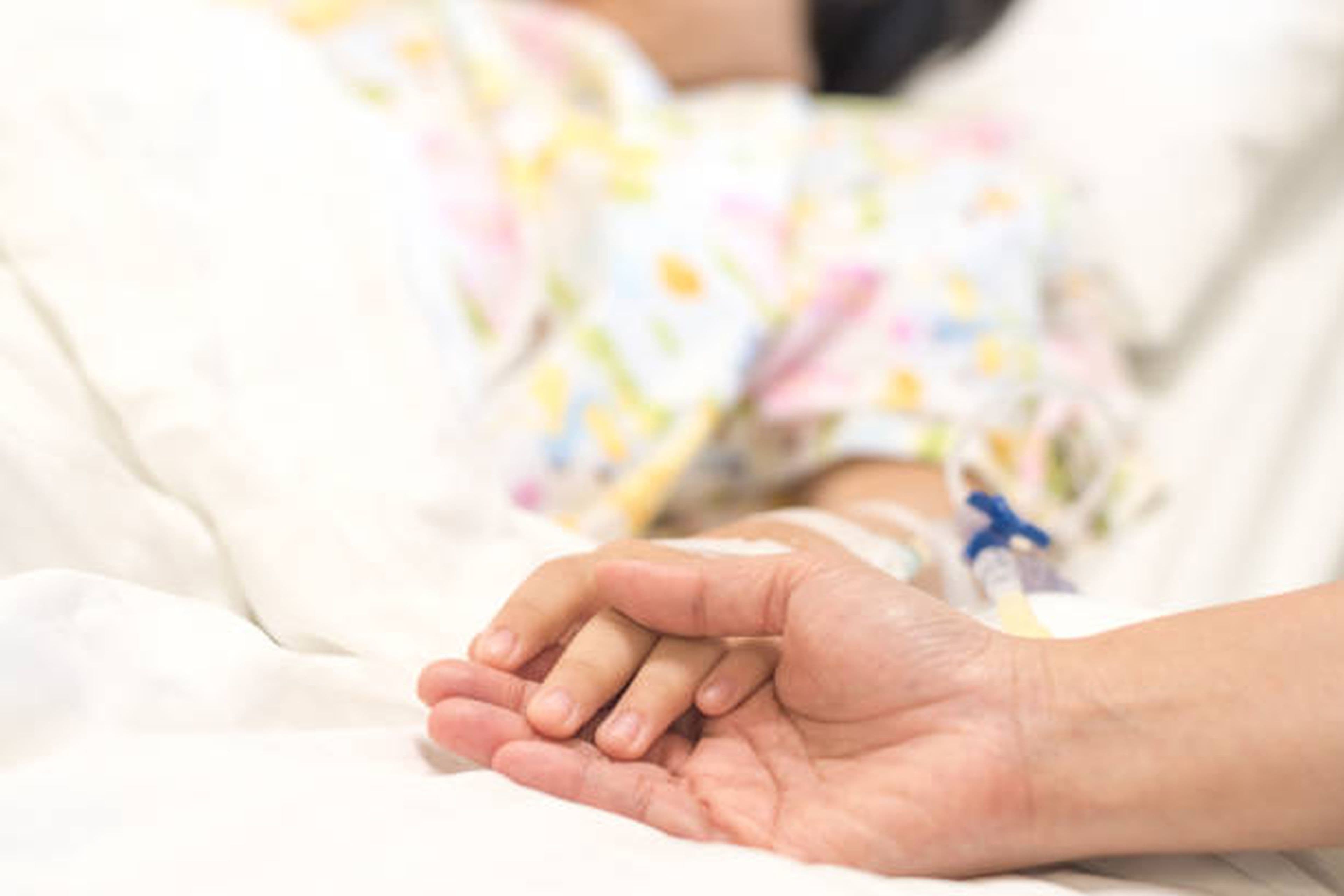 Mână de adult ținând delicat degetul unui copil, simbol al îngrijirii medicale